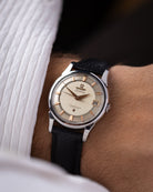 A close-up shot of an Omega Constellation wristwatch with a cream dial, silver-tone case, and black leather strap, worn on a person's wrist.